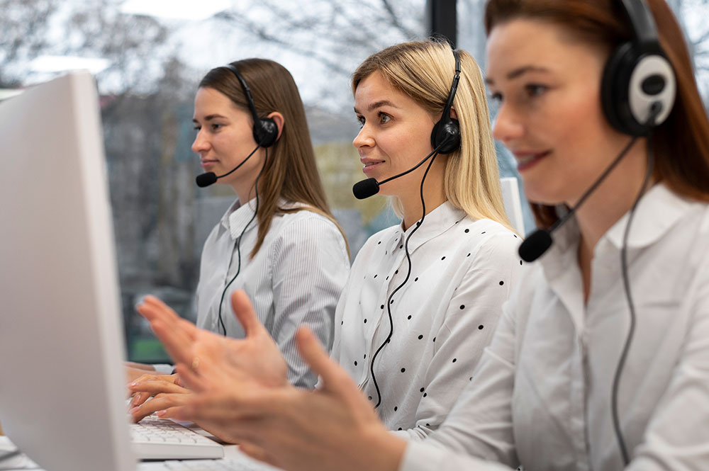 A team of three women wearing headsets, working together in a modern call center environment, focused on providing customer support.